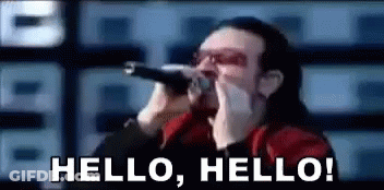 A Man Is Singing Into A Microphone With The Words Hello Hello Behind Him GIF