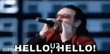 A Man Is Singing Into A Microphone With The Words `` Hello , Hello ! '' Written On It . GIF