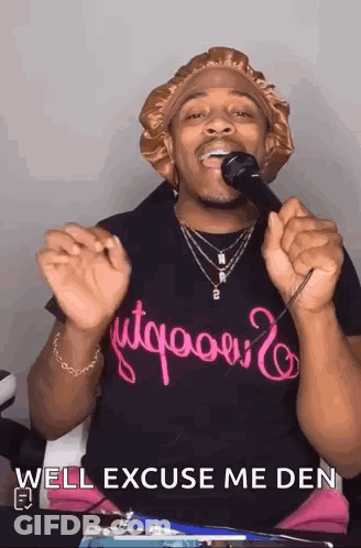 A Man Is Singing Into A Microphone With The Words `` Well Excuse Me Den '' Written On His Shirt . GIF