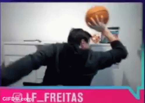 A Man Is Sitting At A Desk Holding A Basketball In His Hand . GIF