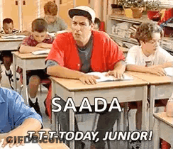 A Man Is Sitting At A Desk In A Classroom With Other Students . GIF