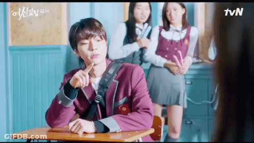 A Man Is Sitting At A Desk In A Classroom With Two Girls Standing Behind Him And A Tvn Logo In The Corner GIF