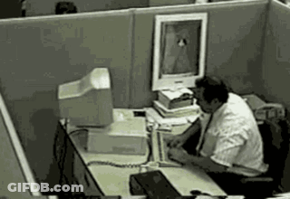 A Man Is Sitting At A Desk In An Office Cubicle With A Computer . GIF