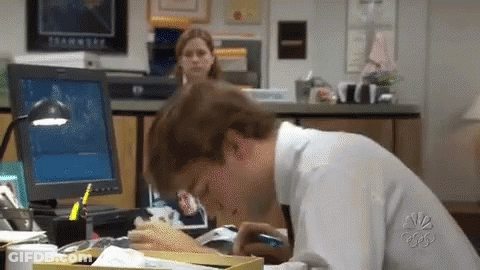 A Man Is Sitting At A Desk In Front Of A Computer And Eating A Sandwich . GIF