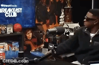 A Man Is Sitting At A Desk In Front Of A Microphone In Front Of A Breakfast Club Sign . GIF