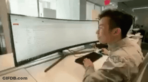 A Man Is Sitting At A Desk Looking At A Computer Monitor . GIF