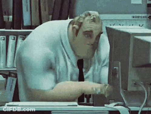 A Man Is Sitting At A Desk Looking At A Computer Monitor . GIF