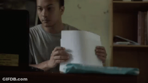 A Man Is Sitting At A Desk Looking At A Piece Of Paper . GIF