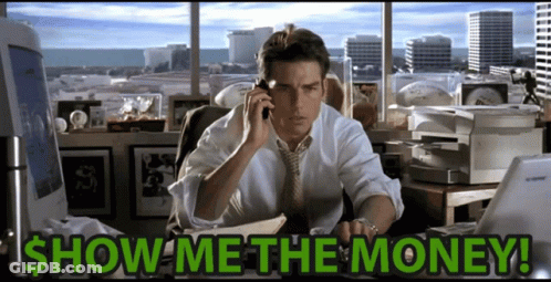 A Man Is Sitting At A Desk Talking On A Cell Phone With The Words Show Me The Money Written Below Him GIF