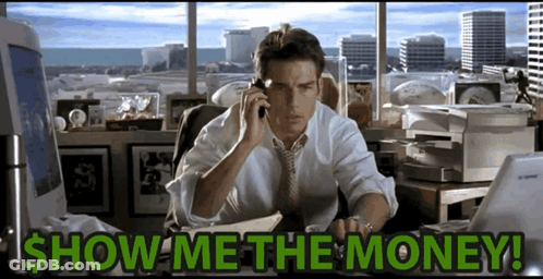 A Man Is Sitting At A Desk Talking On A Cell Phone With The Words Show Me The Money Written Below Him GIF