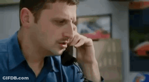 A Man Is Sitting At A Desk Talking On A Cell Phone . GIF