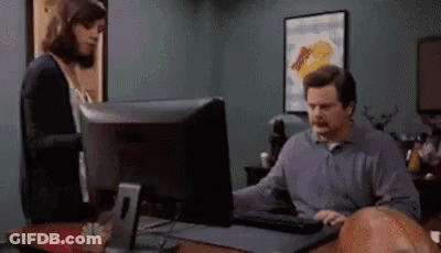 A Man Is Sitting At A Desk Using A Computer While A Woman Looks On . GIF