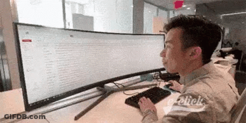 A Man Is Sitting At A Desk Using A Computer With A Large Screen . GIF