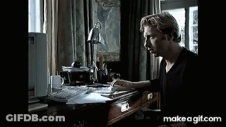 A Man Is Sitting At A Desk With A Computer And A Lamp On It . GIF