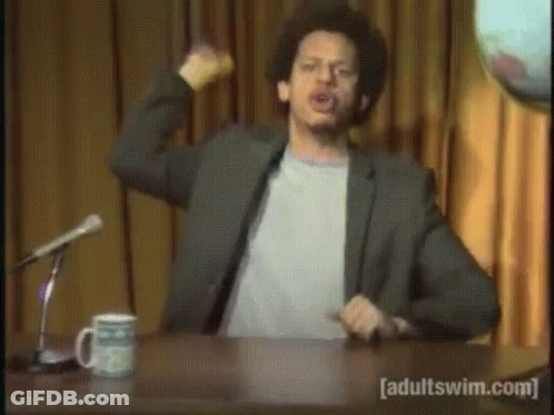 A Man Is Sitting At A Desk With A Microphone And A Mug That Says Adultswim.com GIF