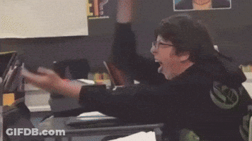 A Man Is Sitting At A Desk With His Arms In The Air Wearing A Black Shirt With The Letter W On It GIF