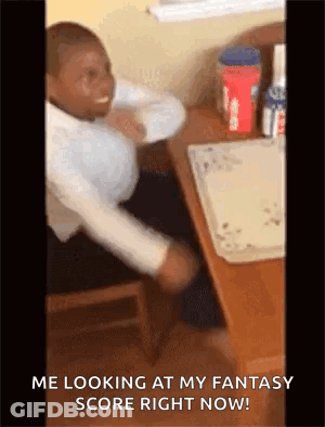 A Man Is Sitting At A Desk With His Arms Outstretched And Looking At His Fantasy Score Right Now . GIF