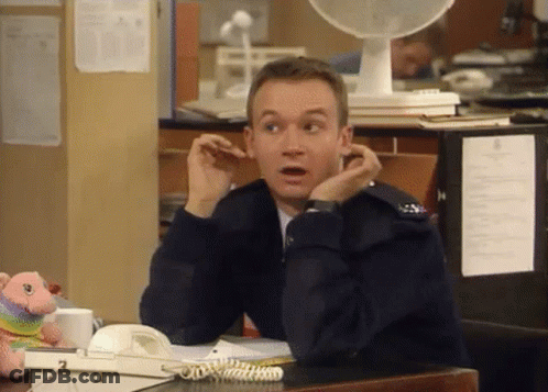 A Man Is Sitting At A Desk With His Hands On His Ears And A Fan Behind Him . GIF