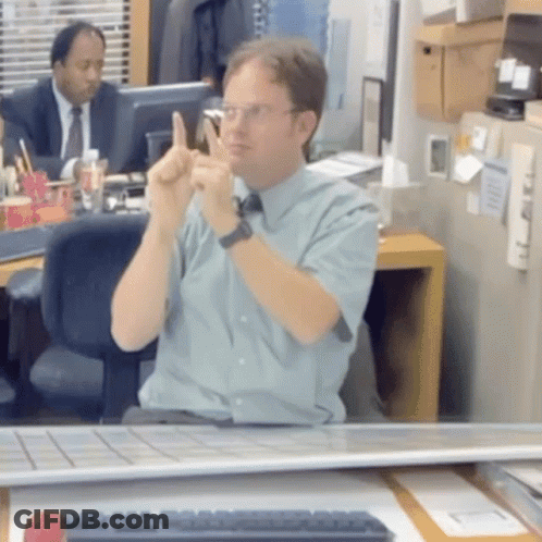 A Man Is Sitting At A Desk With His Hands Up GIF