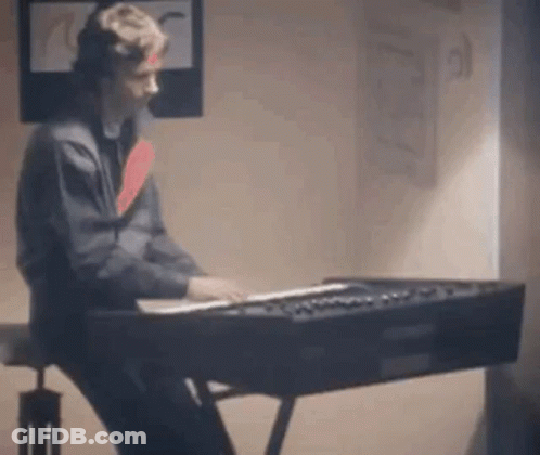 A Man Is Sitting At A Piano In A Room . GIF