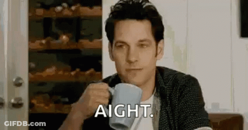 A Man Is Sitting At A Table Drinking A Cup Of Coffee And Saying Aight . GIF