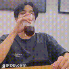 A Man Is Sitting At A Table Drinking A Glass Of Coffee . GIF