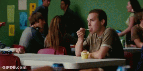 A Man Is Sitting At A Table Eating A Cupcake GIF