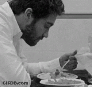 A Man Is Sitting At A Table Eating A Plate Of Food With A Fork . GIF