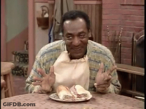 A Man Is Sitting At A Table Eating A Sandwich With A Bag Around His Neck . GIF