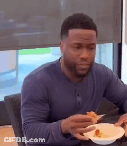 A Man Is Sitting At A Table Eating A Slice Of Pizza . GIF