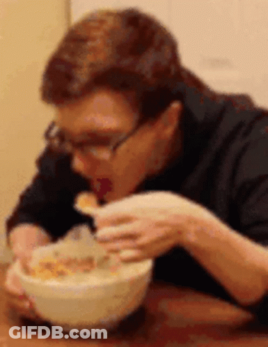 A Man Is Sitting At A Table Eating Cereal From A Bowl . GIF