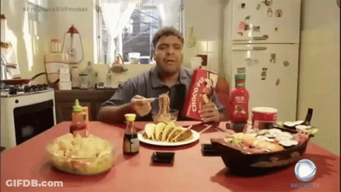 A Man Is Sitting At A Table Eating Food And Holding A Bag That Says Choco Jiu GIF