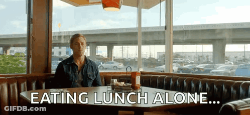 A Man Is Sitting At A Table Eating Lunch Alone GIF