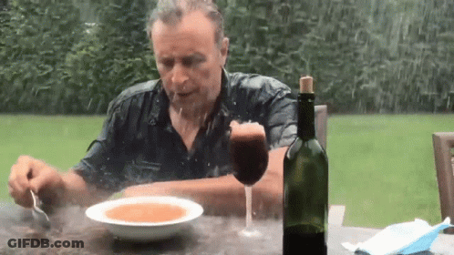 A Man Is Sitting At A Table Eating Soup And Drinking Wine GIF