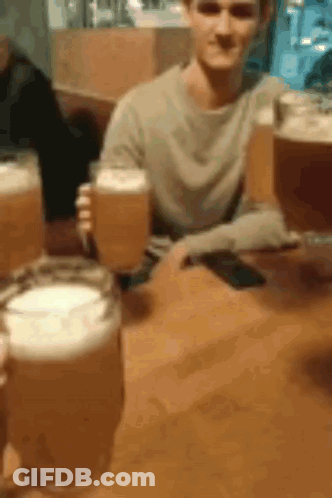 A Man Is Sitting At A Table Holding A Beer Glass . GIF