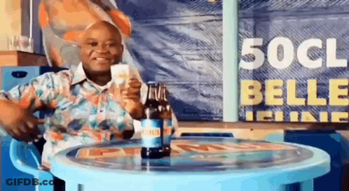 A Man Is Sitting At A Table Holding A Bottle Of Beer And A Glass Of Beer . GIF