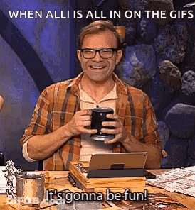 A Man Is Sitting At A Table Holding A Cup Of Coffee And A Tablet Computer . GIF