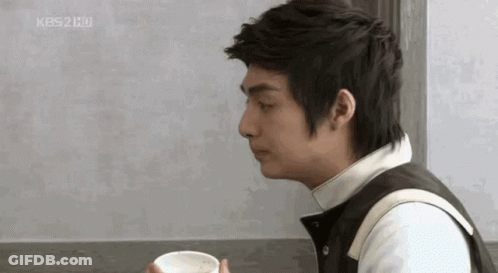 A Man Is Sitting At A Table Holding A Cup Of Coffee In His Hand . GIF