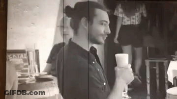 A Man Is Sitting At A Table Holding A Glass Of Wine In A Black And White Photo . GIF