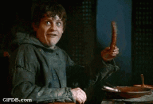 A Man Is Sitting At A Table Holding A Sausage And Making A Funny Face . GIF