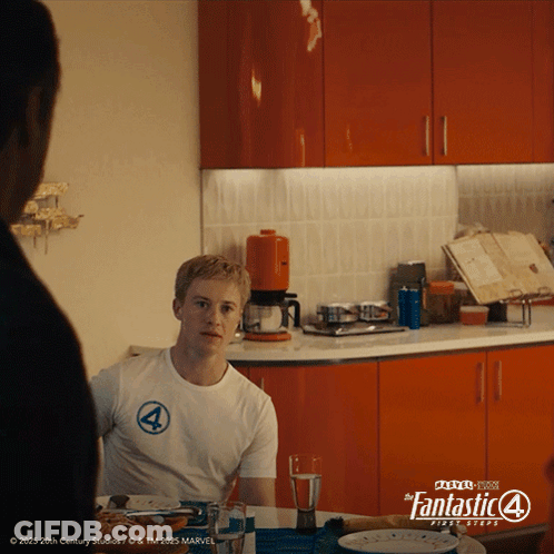 A Man Is Sitting At A Table In A Kitchen Wearing A Fantastic 4 Shirt GIF