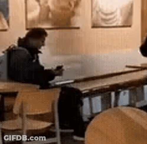 A Man Is Sitting At A Table In A Restaurant Looking At His Phone GIF