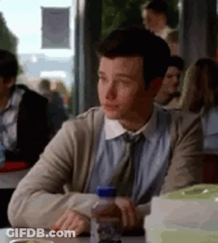 A Man Is Sitting At A Table In A Restaurant With A Bottle Of Water In His Hand . GIF