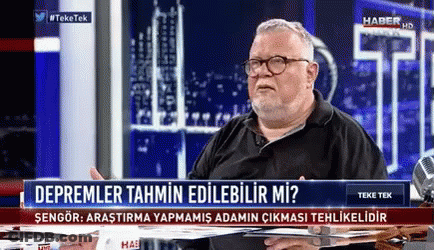 A Man Is Sitting At A Table In Front Of A Sign That Says " Depremler Tahmin Edilebilir Mi " GIF