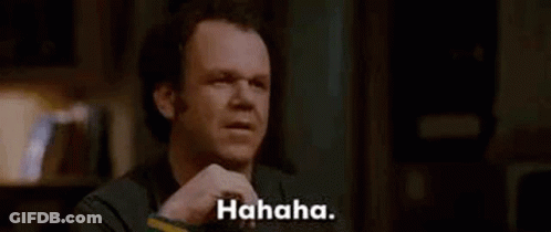 A Man Is Sitting At A Table Laughing While Holding His Hand To His Chin . GIF
