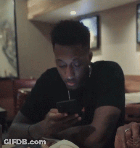 A Man Is Sitting At A Table Looking At His Cell Phone GIF