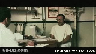 A Man Is Sitting At A Table Talking To Another Man . GIF