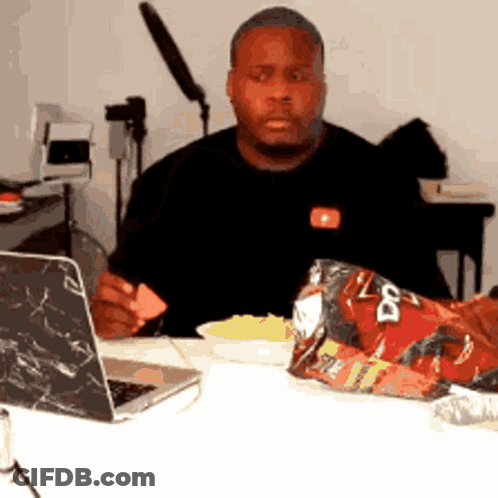 A Man Is Sitting At A Table With A Bag Of Doritos On It GIF