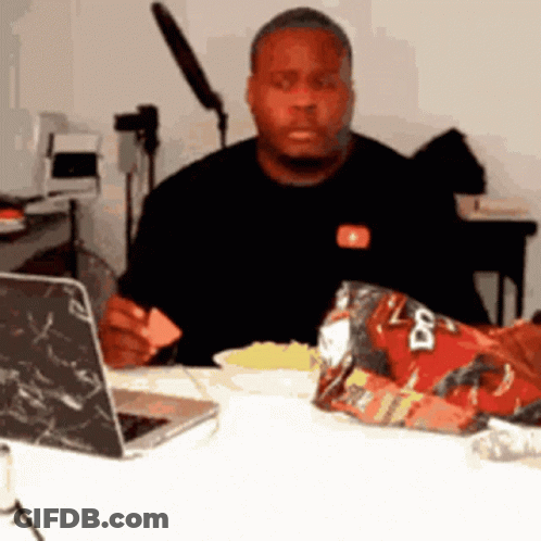A Man Is Sitting At A Table With A Bag Of Doritos On It GIF