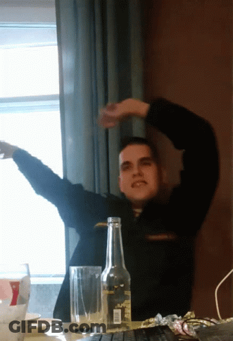A Man Is Sitting At A Table With A Bottle And A Glass GIF